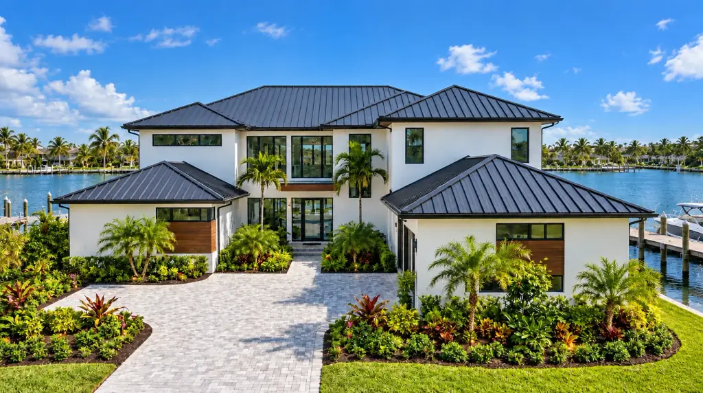 Two-story waterfront South Florida home with a dark standing-seam metal roof under a blue sky